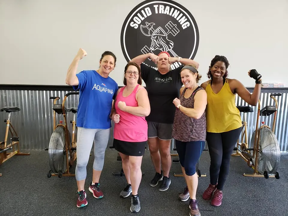 Members flexing under the Solid Training logo wall